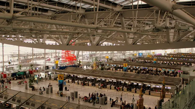 Rows of check-in counters under a wide departures board in a large airport terminal hall.