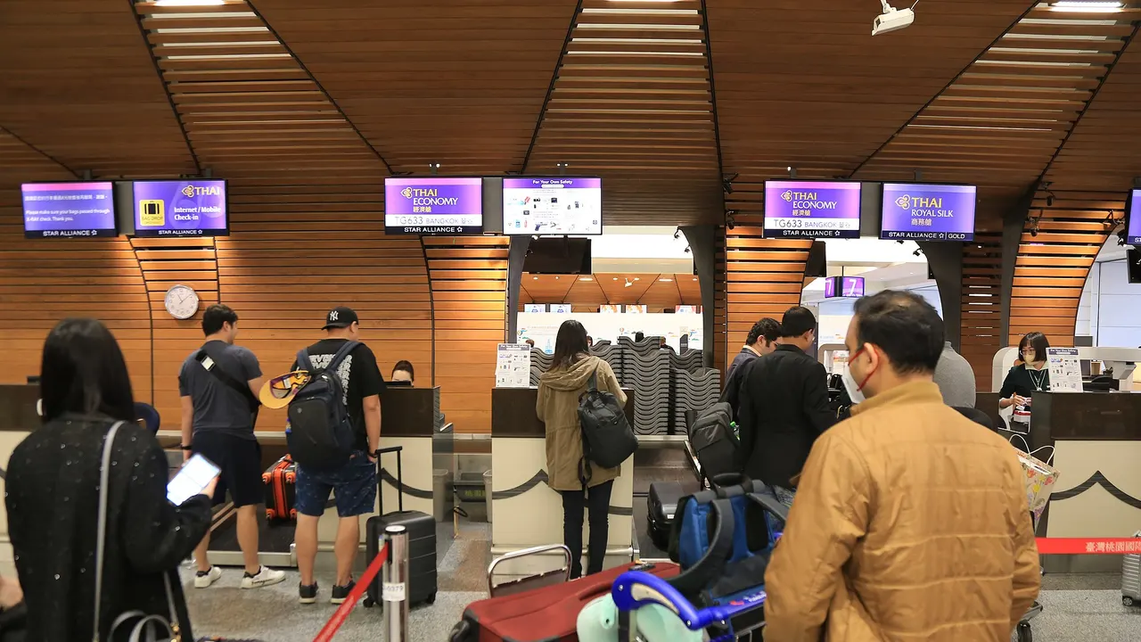 Travellers queueing with luggage in a bright airport terminal, seen from behind