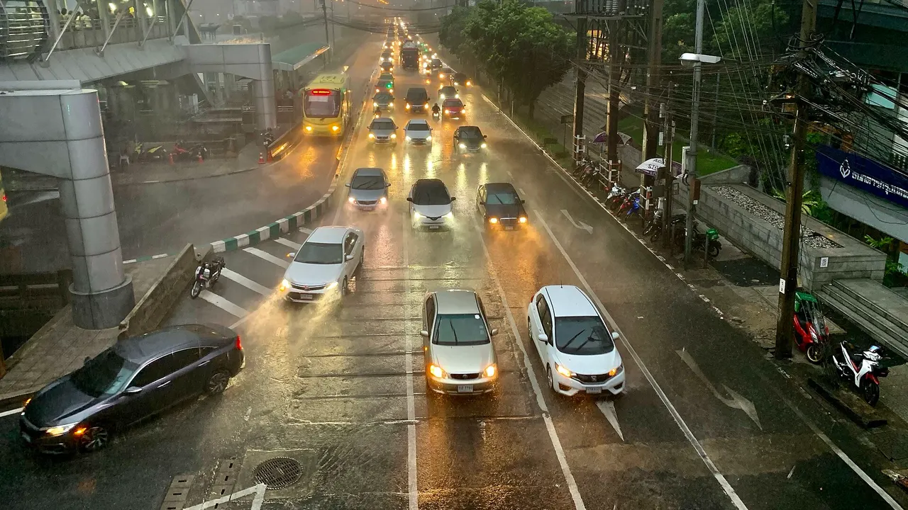 Wasserbedeckte Straße vor Ladenzeilen nach starkem Regen, mit Motorrollern am Straßenrand und grauem Himmel.