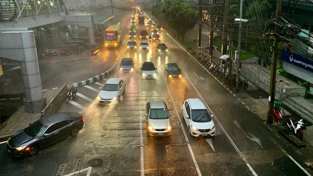 Wasserbedeckte Straße vor Ladenzeilen nach starkem Regen, mit Motorrollern am Straßenrand und grauem Himmel.
