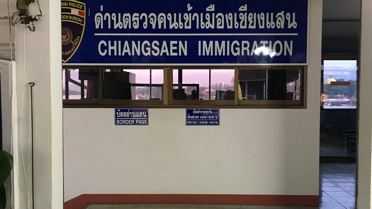 Passport-control desks under bright lighting in an airport arrivals hall, with travellers queuing with their documents.