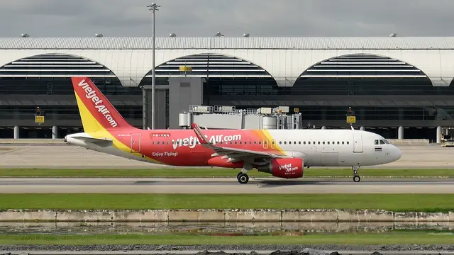 Ein zweistrahliges Langstreckenflugzeug in der Kurve über dem Meer, Tragflächen nach oben gebogen, im Hintergrund grüne tropische Hügel.